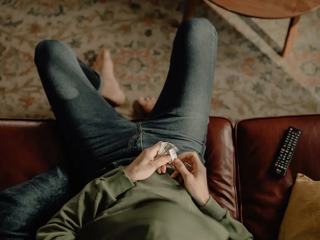 Person in Gray Jacket and Black Pants Sitting on Brown Leather Couch