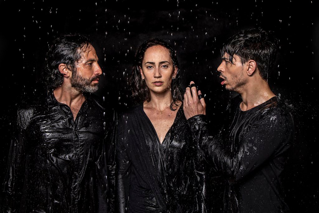 Photogenic talented artists wearing wet black clothes standing in studio under water drops