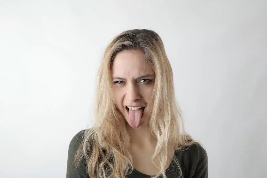 A playful woman with blond hair makes a funny face, sticking her tongue out on a white background.