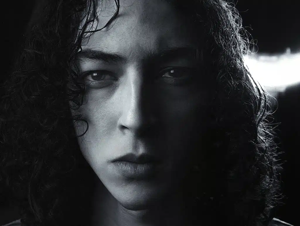 Close-up black and white portrait of a young man with curly hair in London studio lighting.