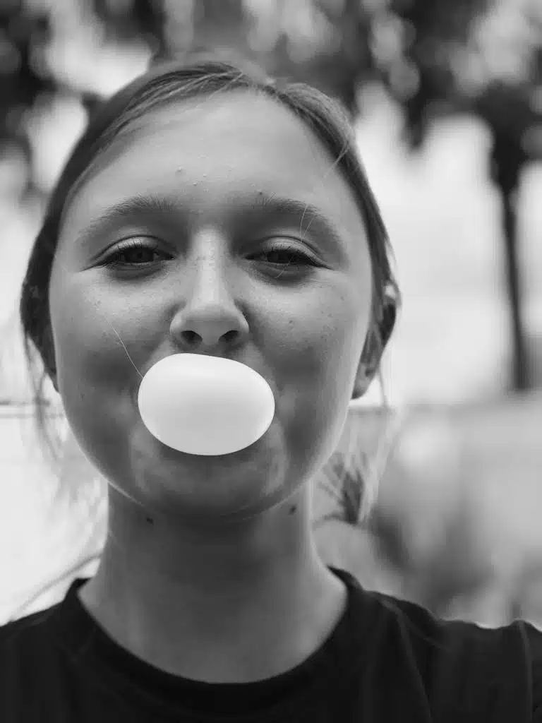 Close-up of a young woman blowing a bubble gum ball in black and white.
