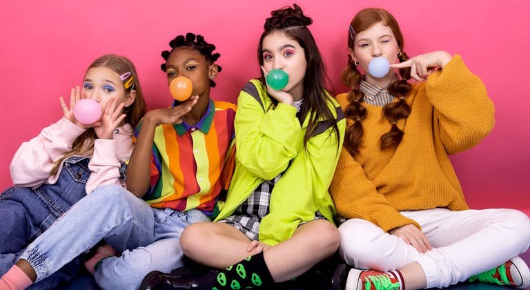 Colorful portrait of teenagers blowing bubble gum against a vibrant pink backdrop, showcasing fun and friendship.