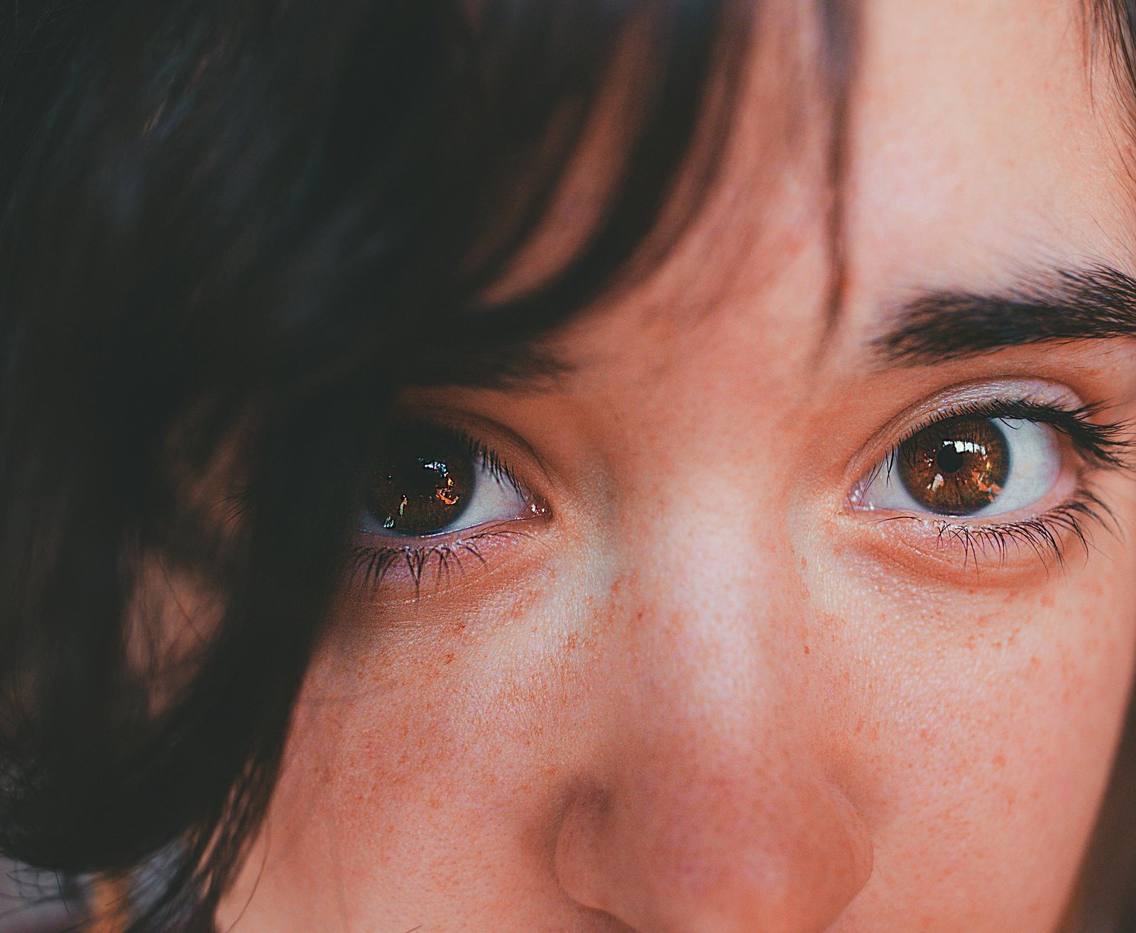 Intimate close-up portrait focusing on expressive hazel eyes and natural freckles.