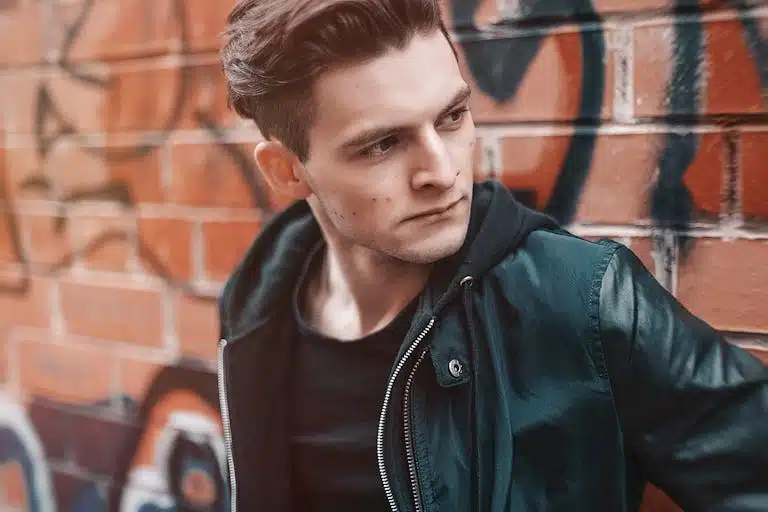 Portrait of a stylish young man posing in front of graffiti-covered wall.