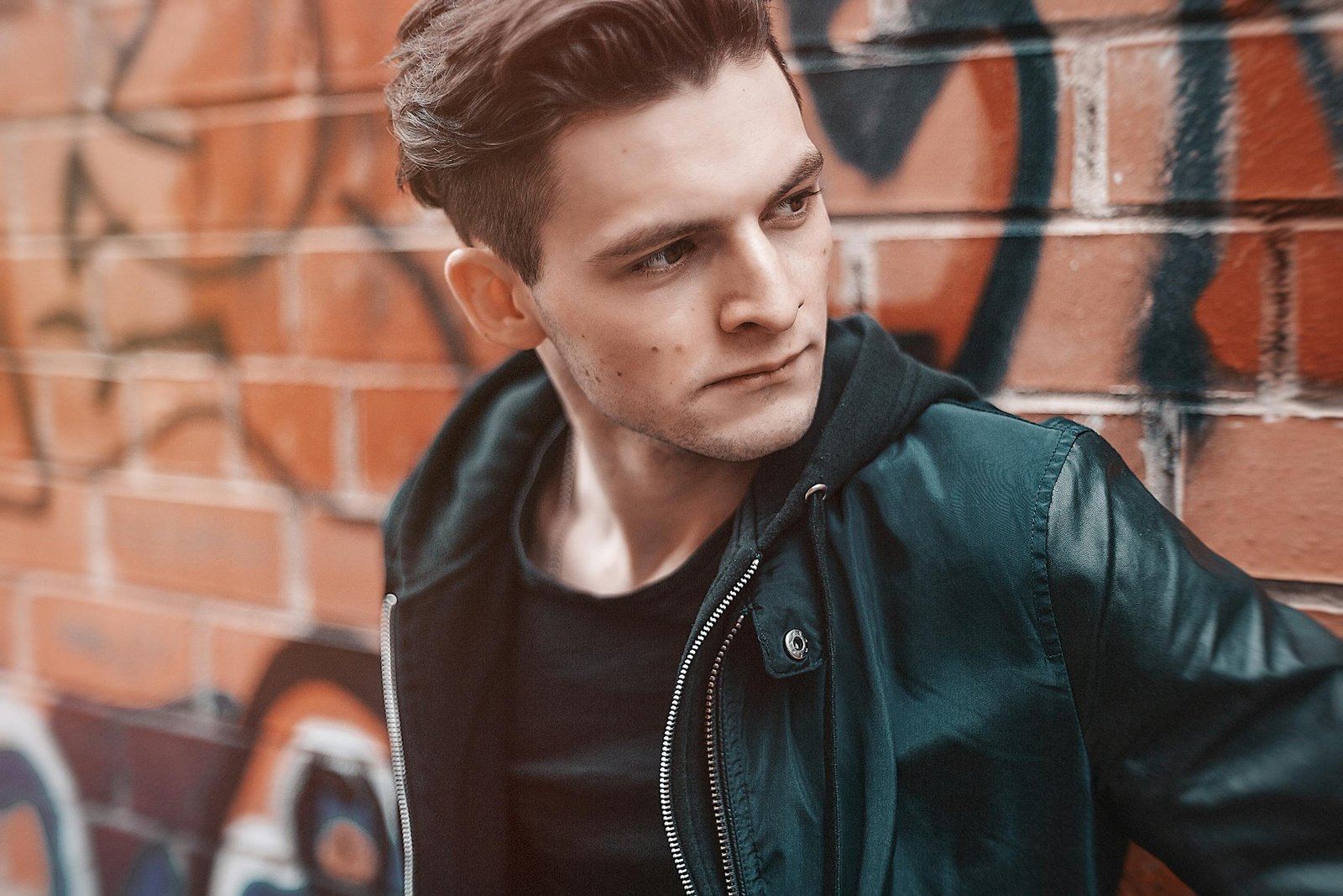 Portrait of a stylish young man posing in front of graffiti-covered wall.