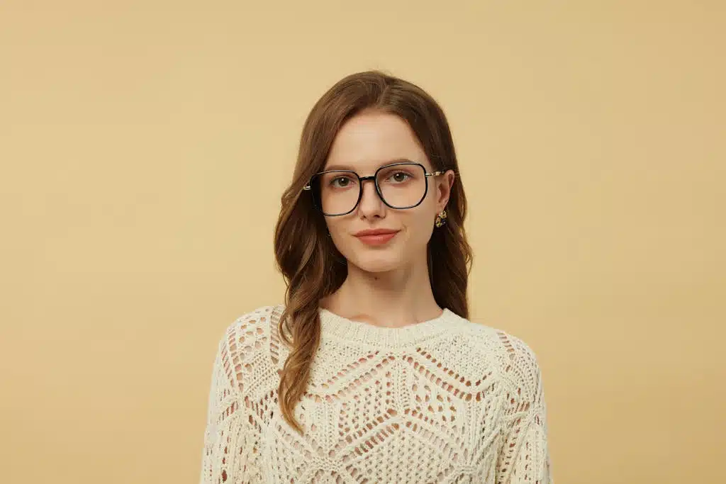 Portrait of a woman in chic glasses and knit sweater against a neutral background.