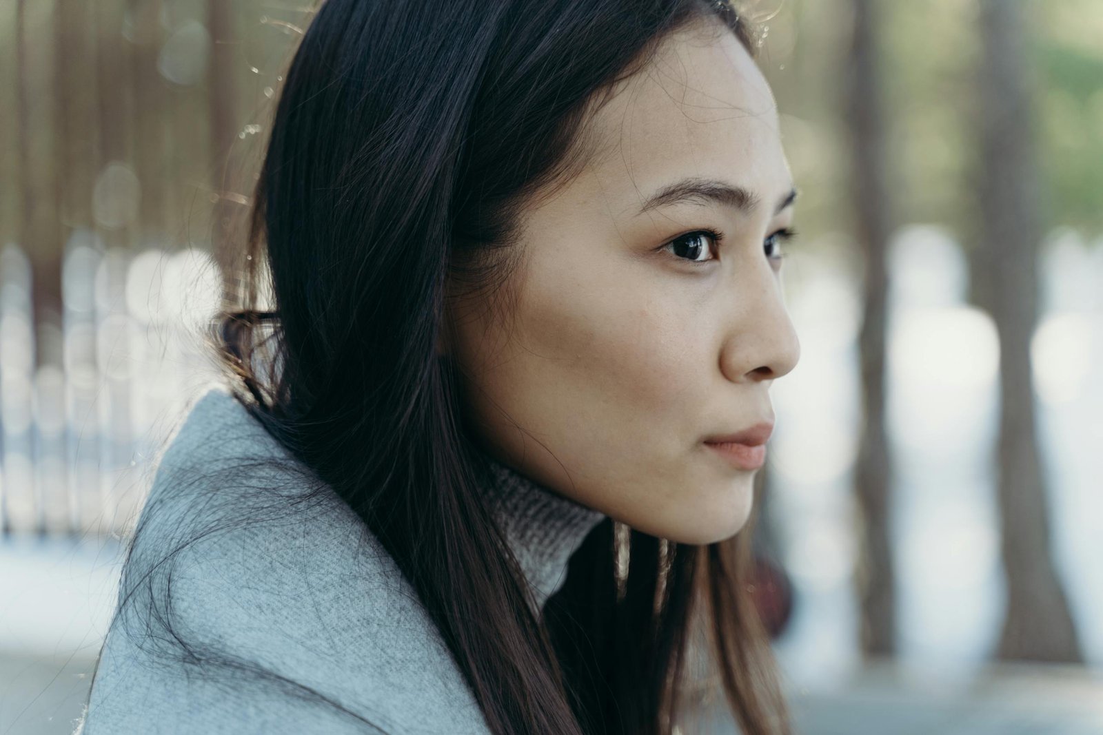 Serene side profile of a woman with long hair wearing a scarf outdoors.