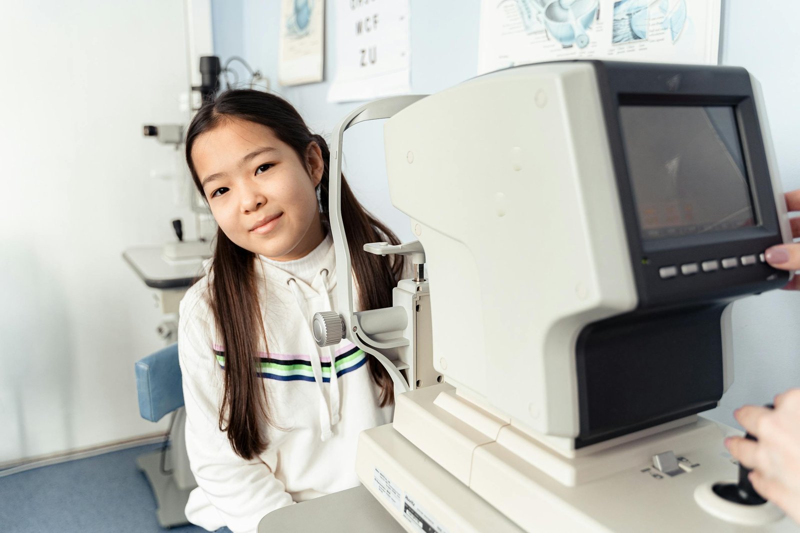 Young girl receiving an eye test with autorefractor in a clinical setting.