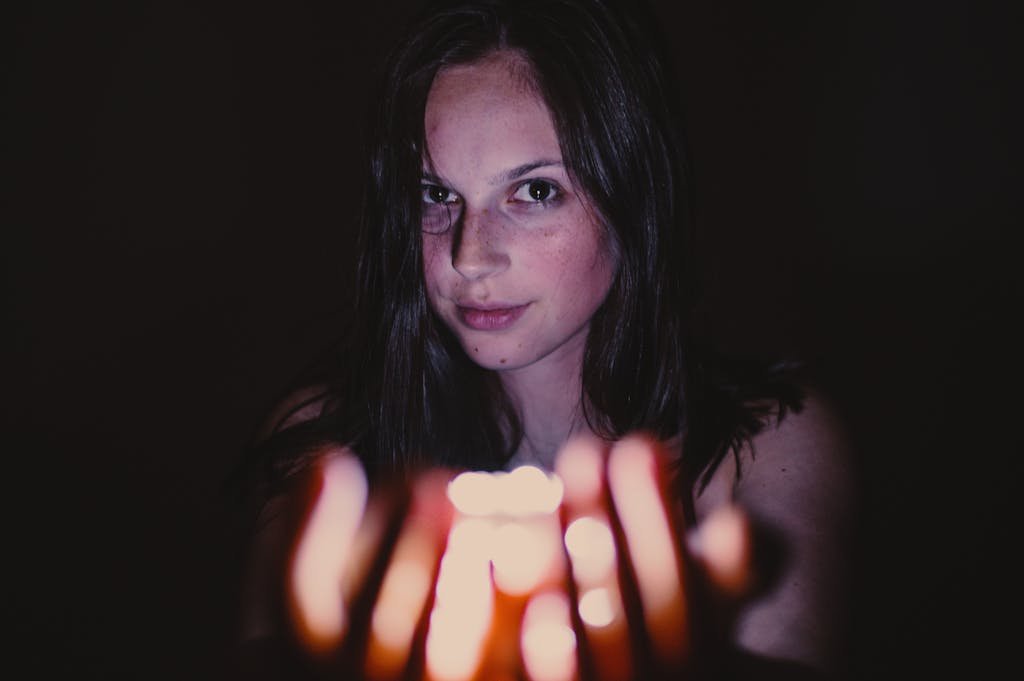 A young woman holding a glowing candle in a dark setting, creating a mysterious mood.