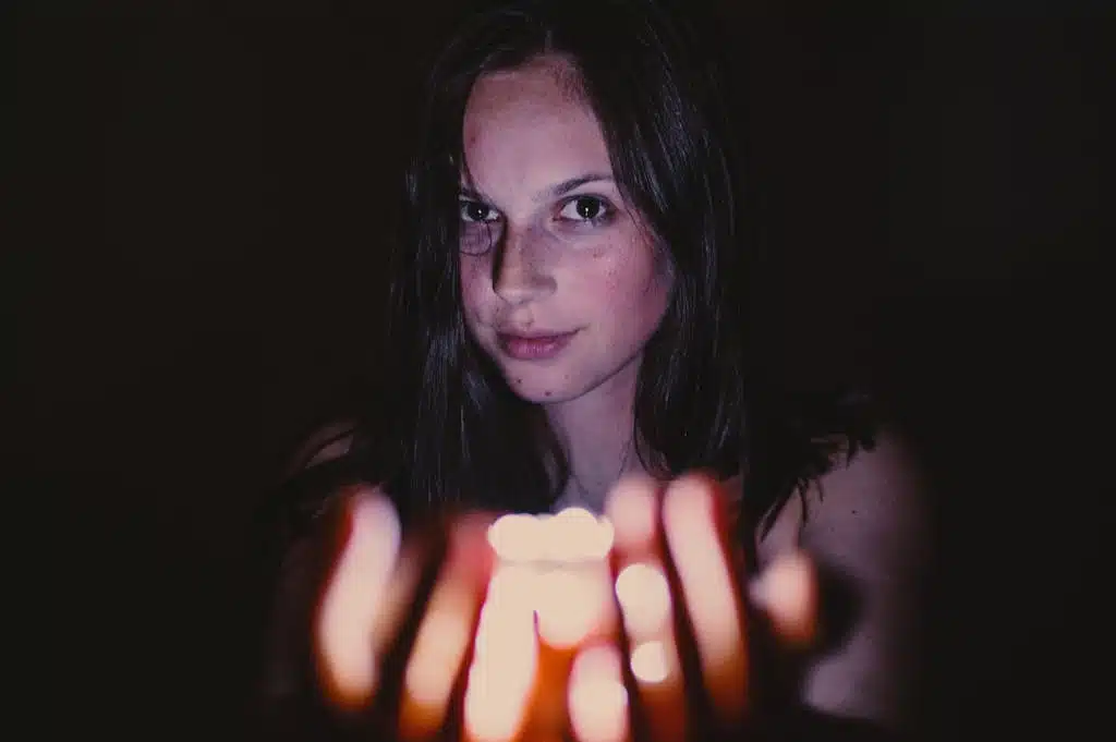 A young woman holding a glowing candle in a dark setting, creating a mysterious mood.