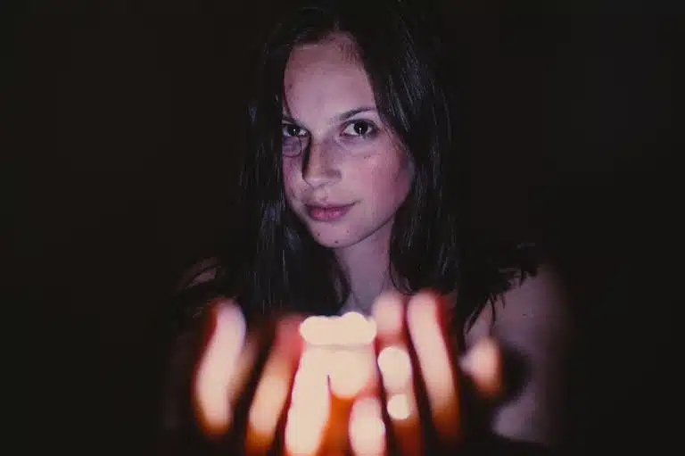 A young woman holding a glowing candle in a dark setting, creating a mysterious mood.