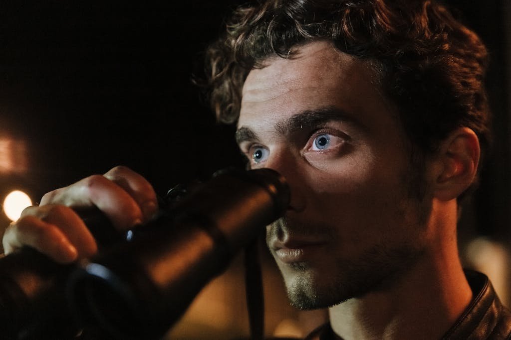 Close-up of a man with intense gaze using binoculars during night time observation.