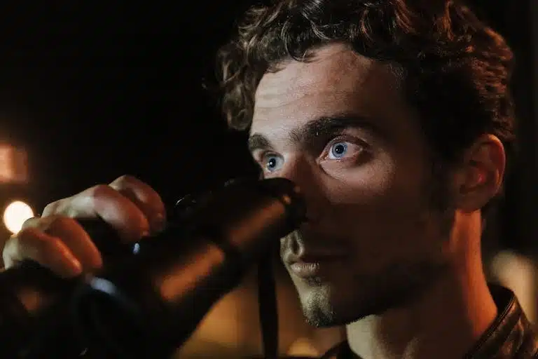 Close-up of a man with intense gaze using binoculars during night time observation.