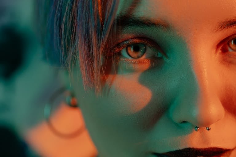 Close-up of a woman with a nose piercing, vibrant lighting and artistic shadows.
