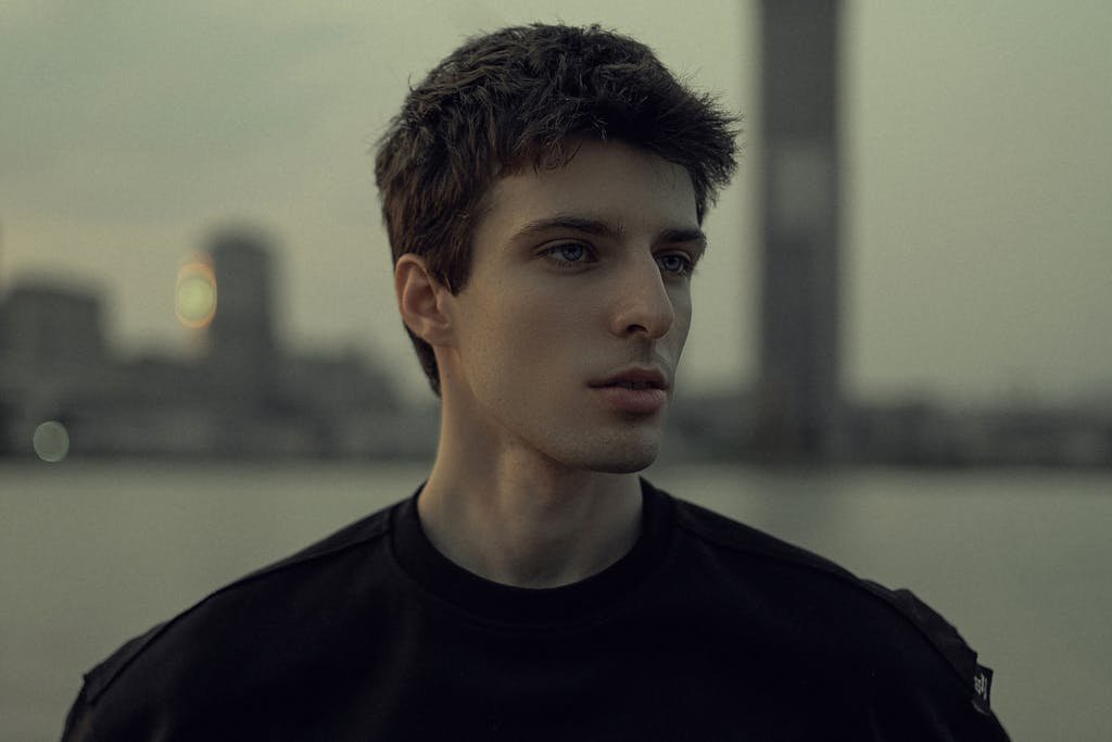 Portrait of a young man with a city skyline at twilight, capturing a moody and contemplative atmosphere.