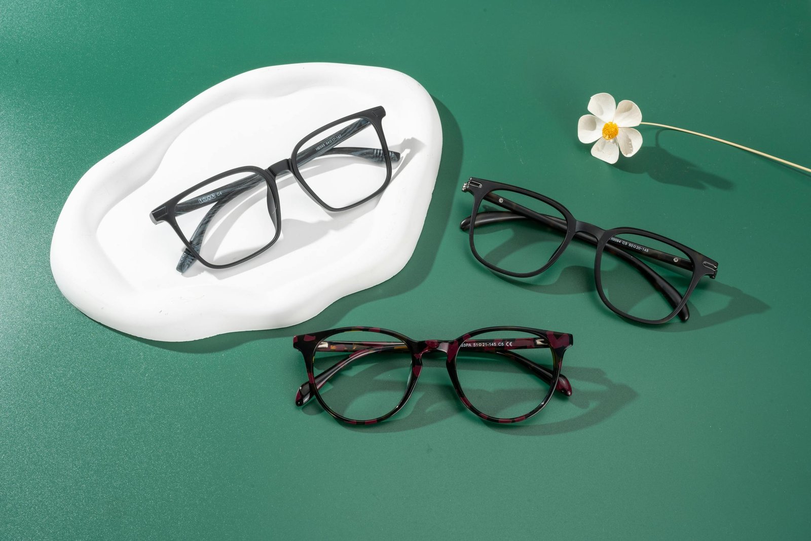 Modern eyeglasses arranged on a green surface with delicate floral decor.