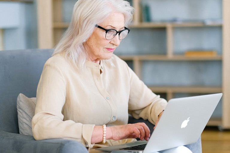 Senior woman sitting indoors using a laptop for online activities.