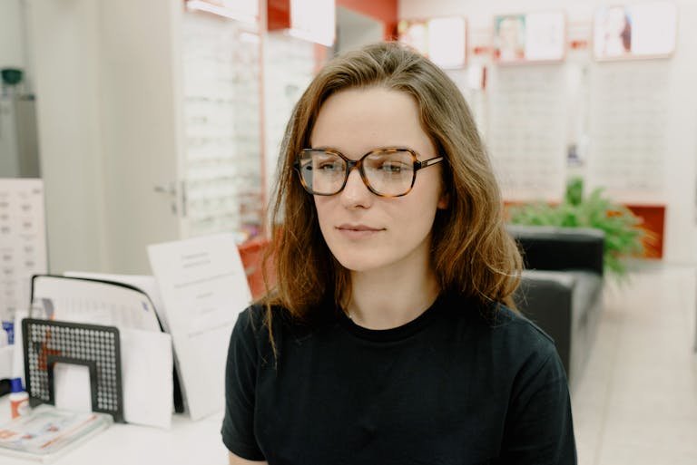 A woman examines her new glasses inside an optical store, focusing on choosing eyewear.